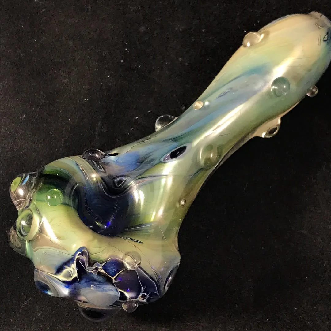 Close-up of a colorful glass pipe with swirls of green, blue, and metallic hues on a black surface.