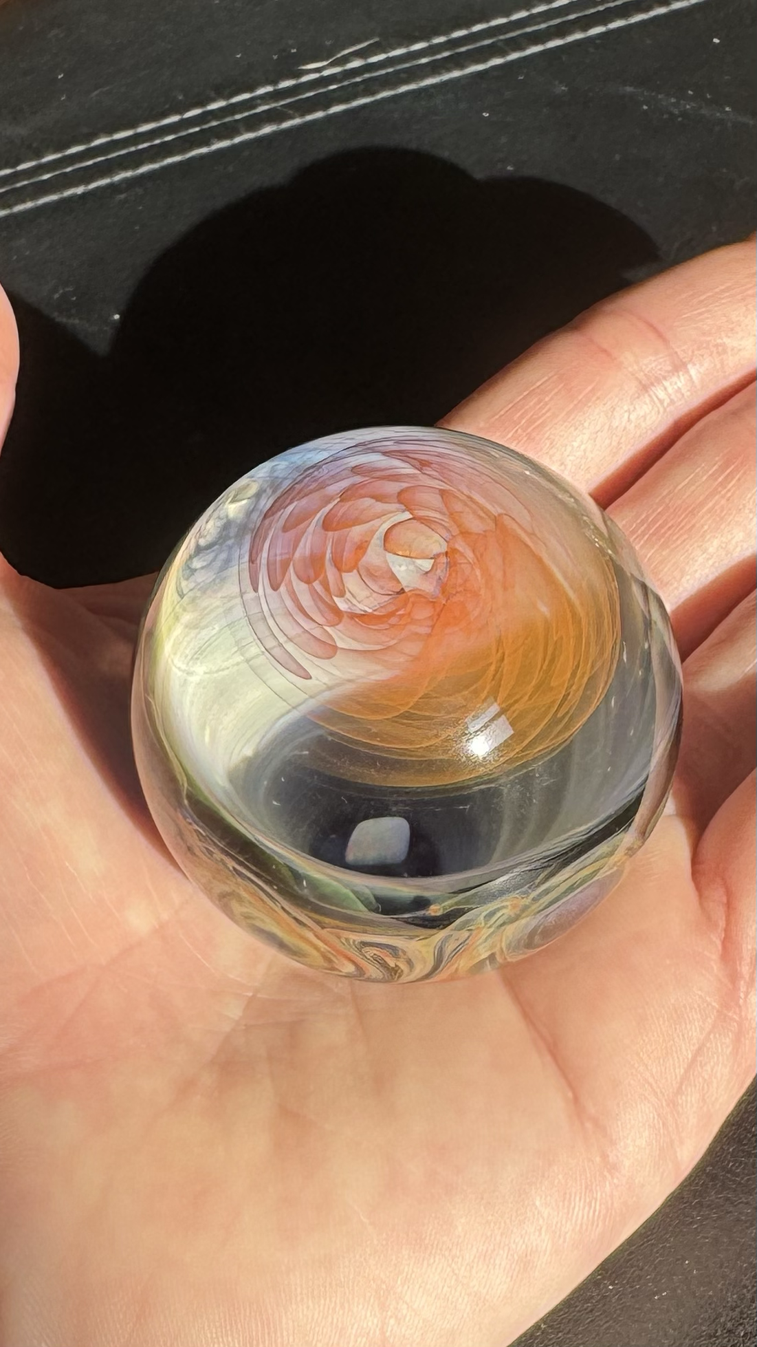 Close-up of a person's hand holding a glass marble with orange, yellow, and red swirling patterns inside.