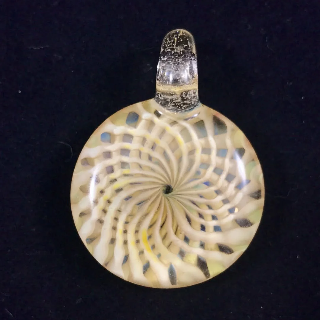 A glass pendant with an intricate spiral pattern inside, resembling a psychedelic or abstract design, set against a black background.