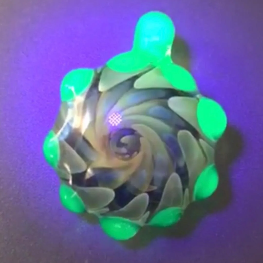 Spinning glass art piece with green glowing tips on a purple background.