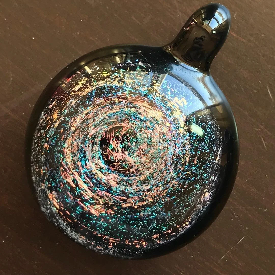 A decorative black glass paperweight with an iridescent, swirling pattern inside.