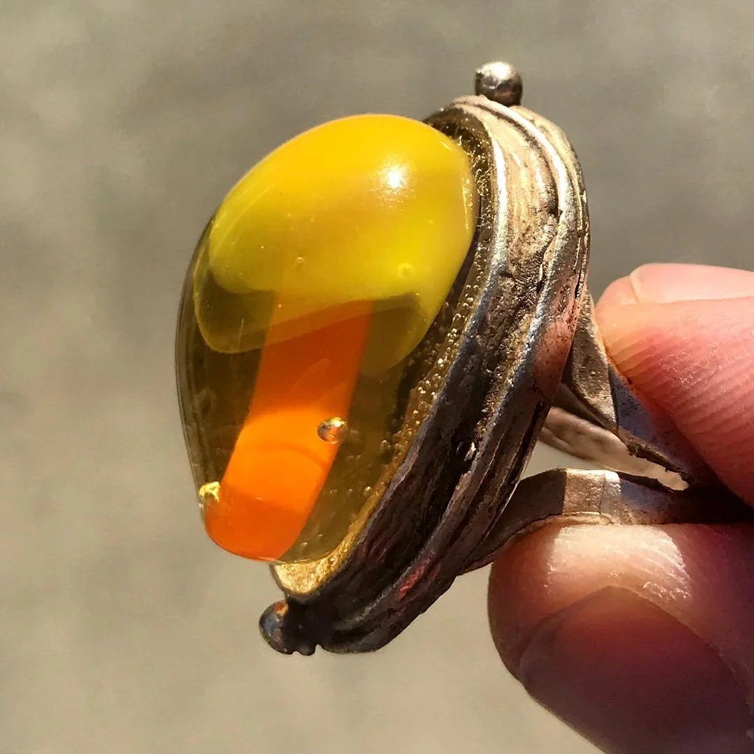 Close-up of a vintage pocket watch with a yellow and orange glass cover, showing the inner workings and the watch's rim, held in a person's hand.
