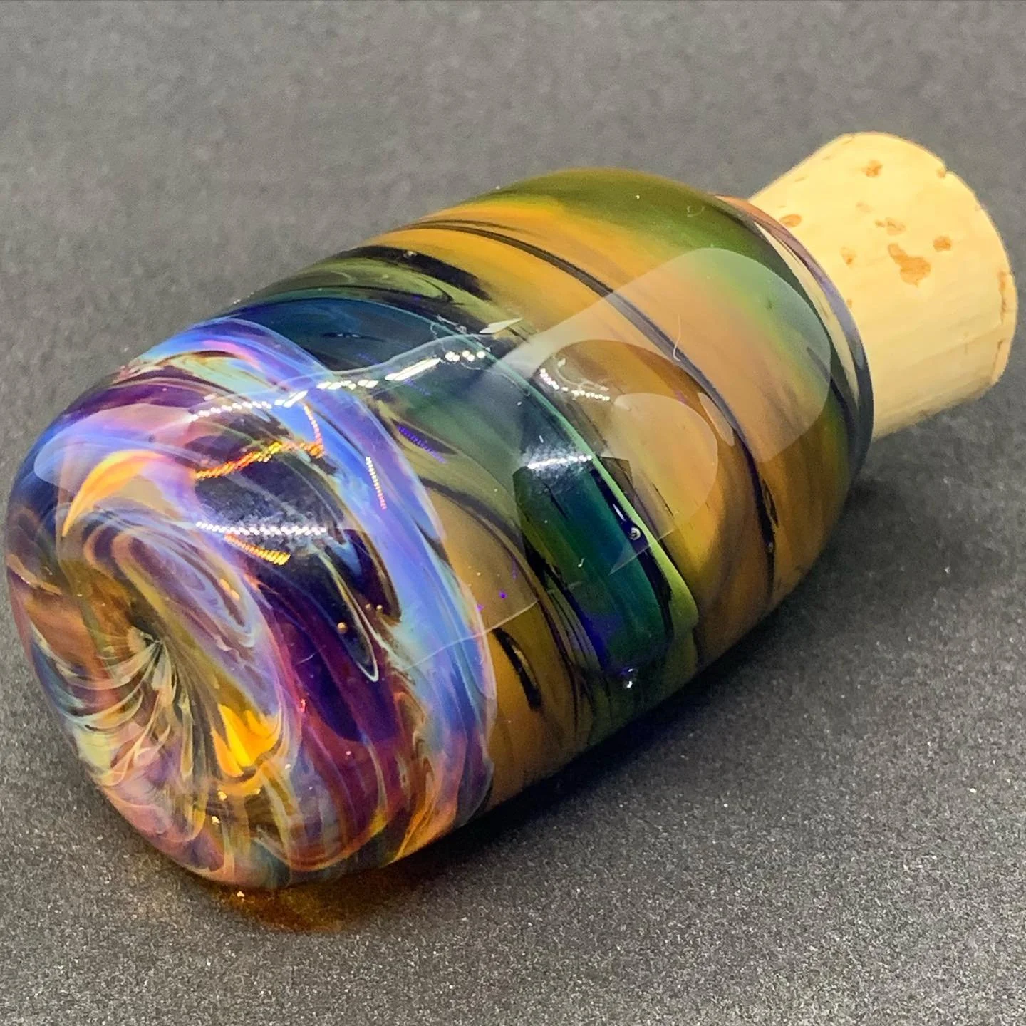 Colorful glass marble with swirling patterns, attached to a cork, resting on a dark surface.