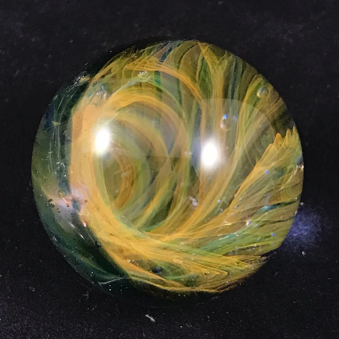 A colorful glass marble with swirling yellow, green, and blue patterns on a black background