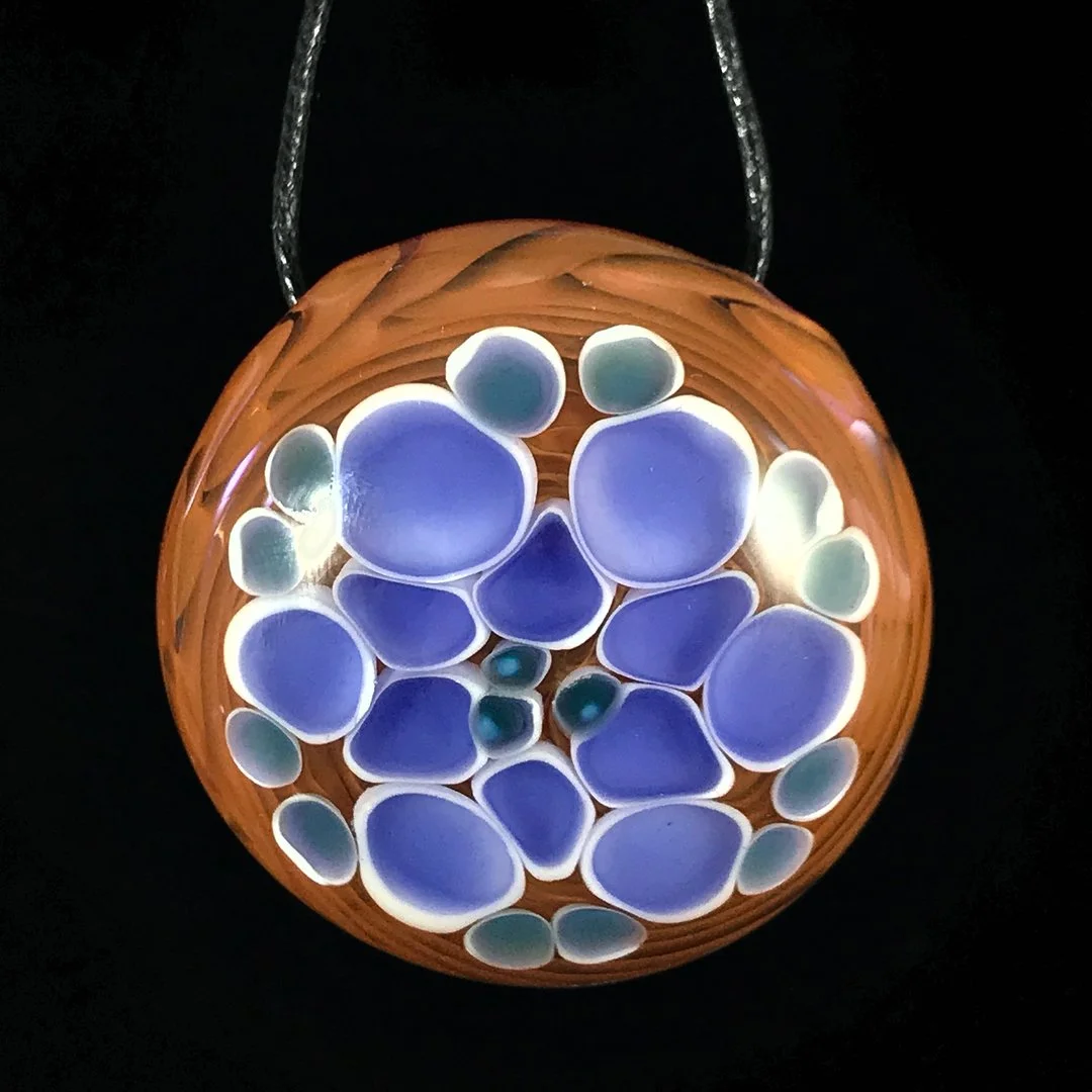 Top-down view of a circular wooden chandelier with multiple rounded glass orbs in shades of blue and green, illuminated against a dark background.