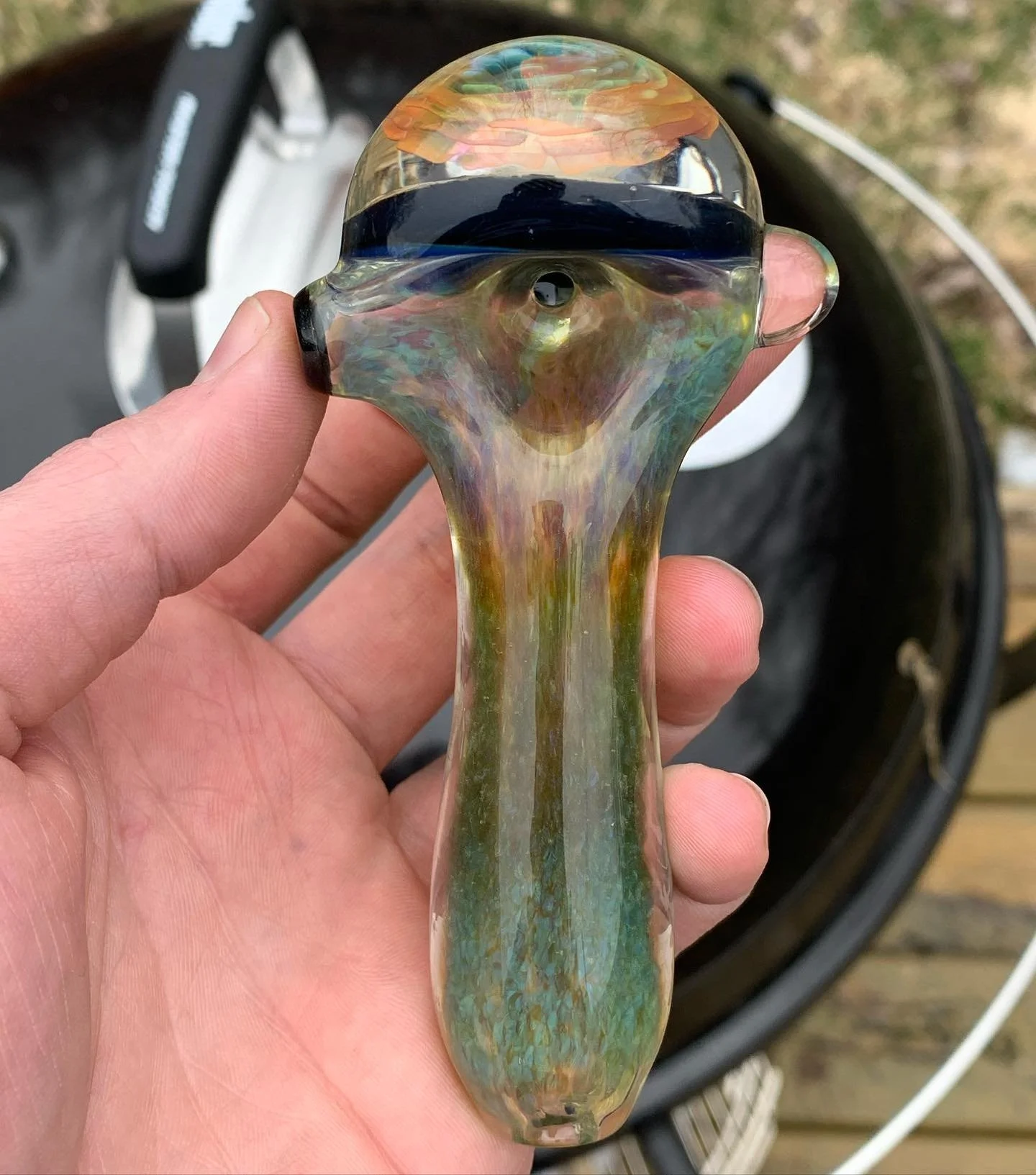 A person holding a glass pipe with an eye design in the bowl, featuring iridescent colors and a black stripe on the top.