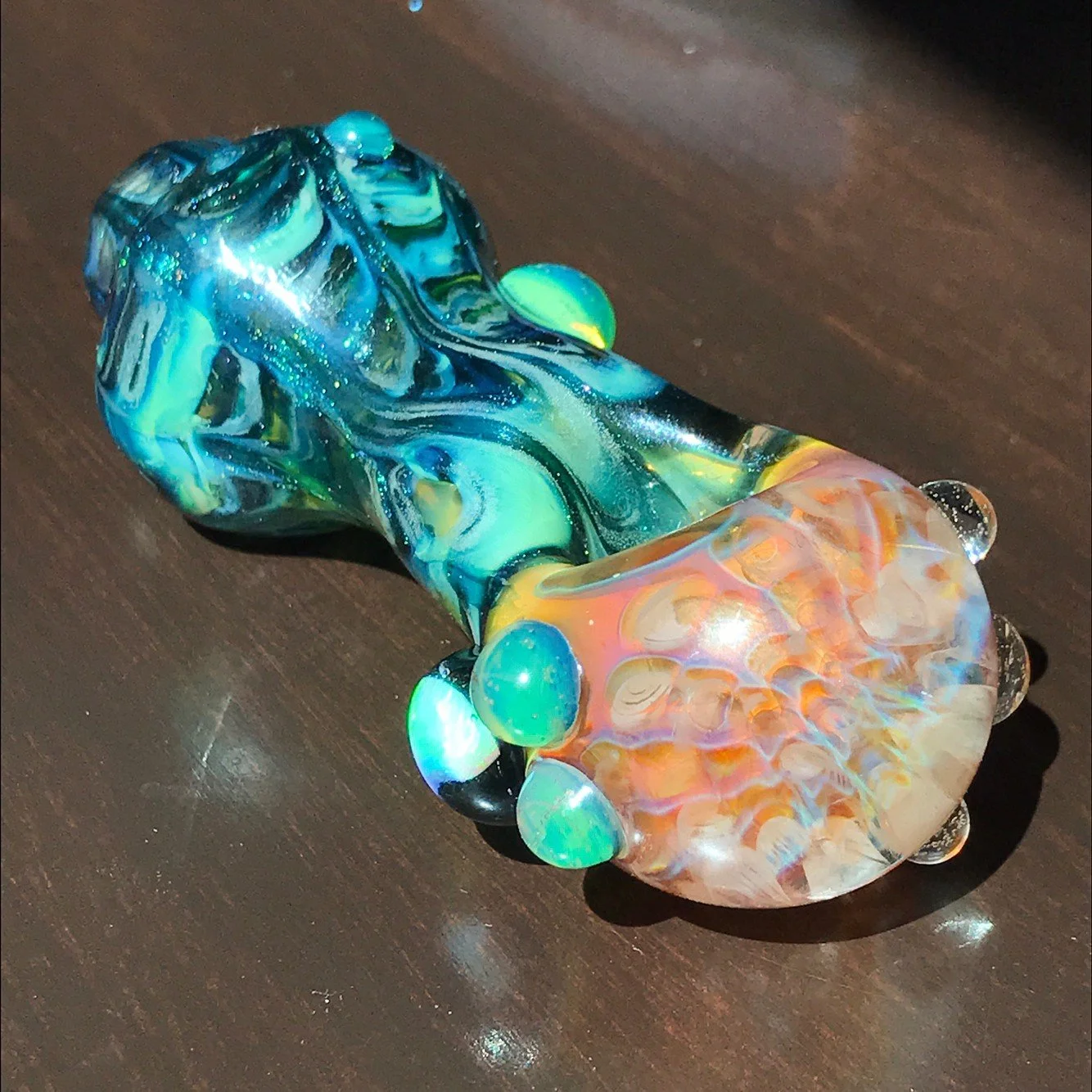 Colorful glass pipe with blue, green, orange, and yellow swirls, lying on a dark wooden surface.