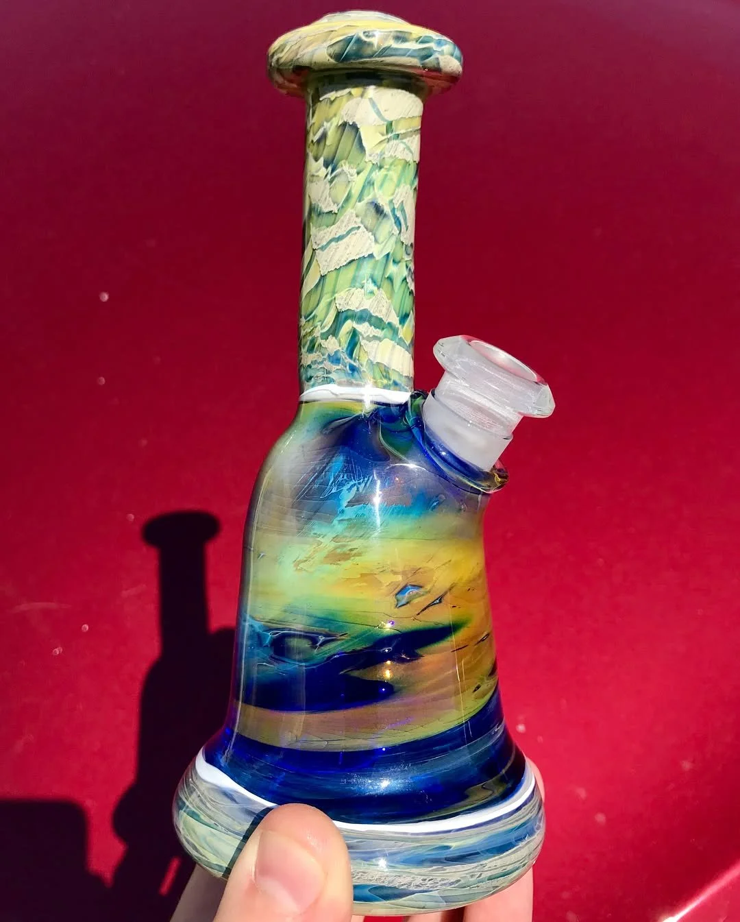 Colorful glass bong with a marble pattern, held by a hand against a red background.