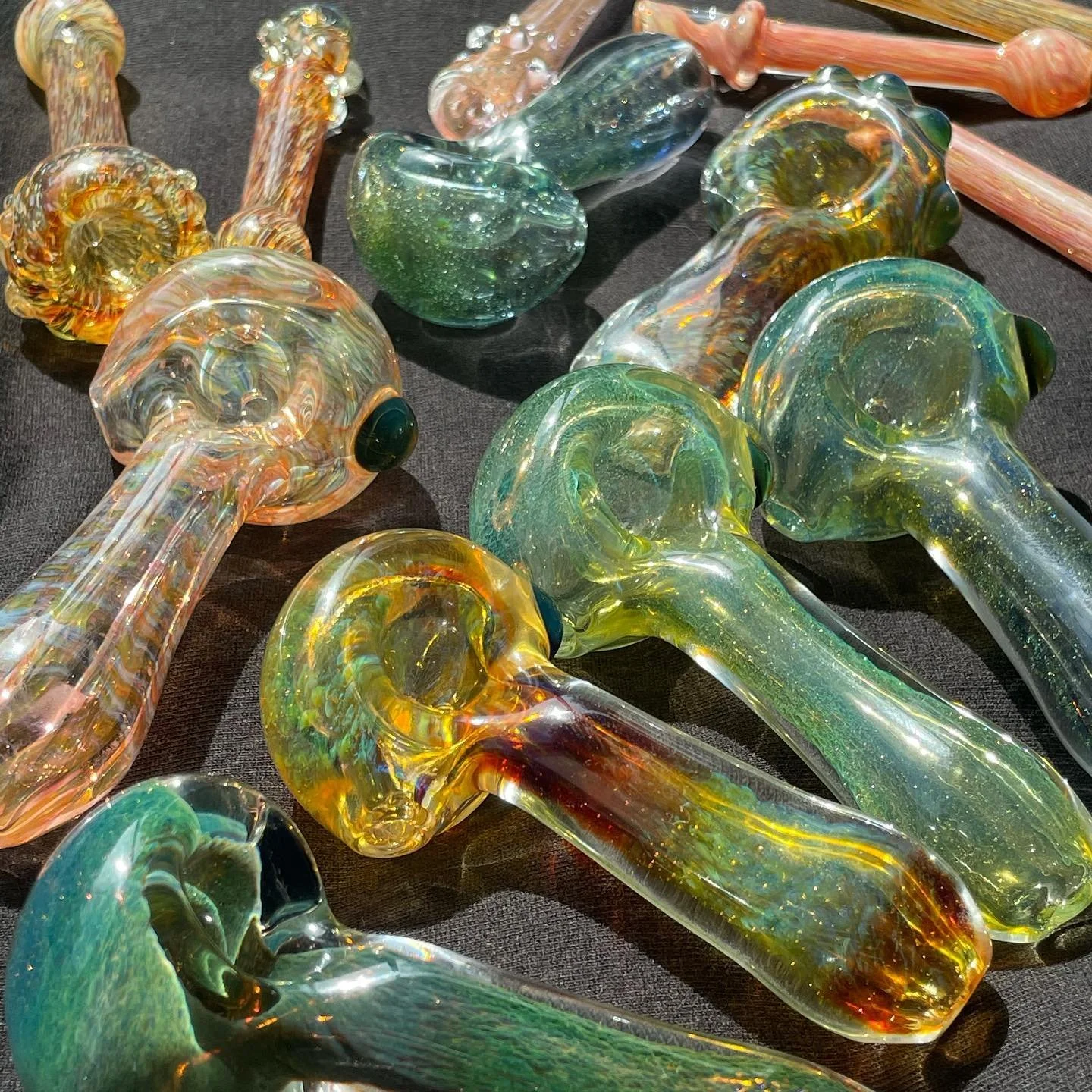 Colorful glass smoking pipes with swirls of green, orange, pink, and yellow, laid out on a black surface.
