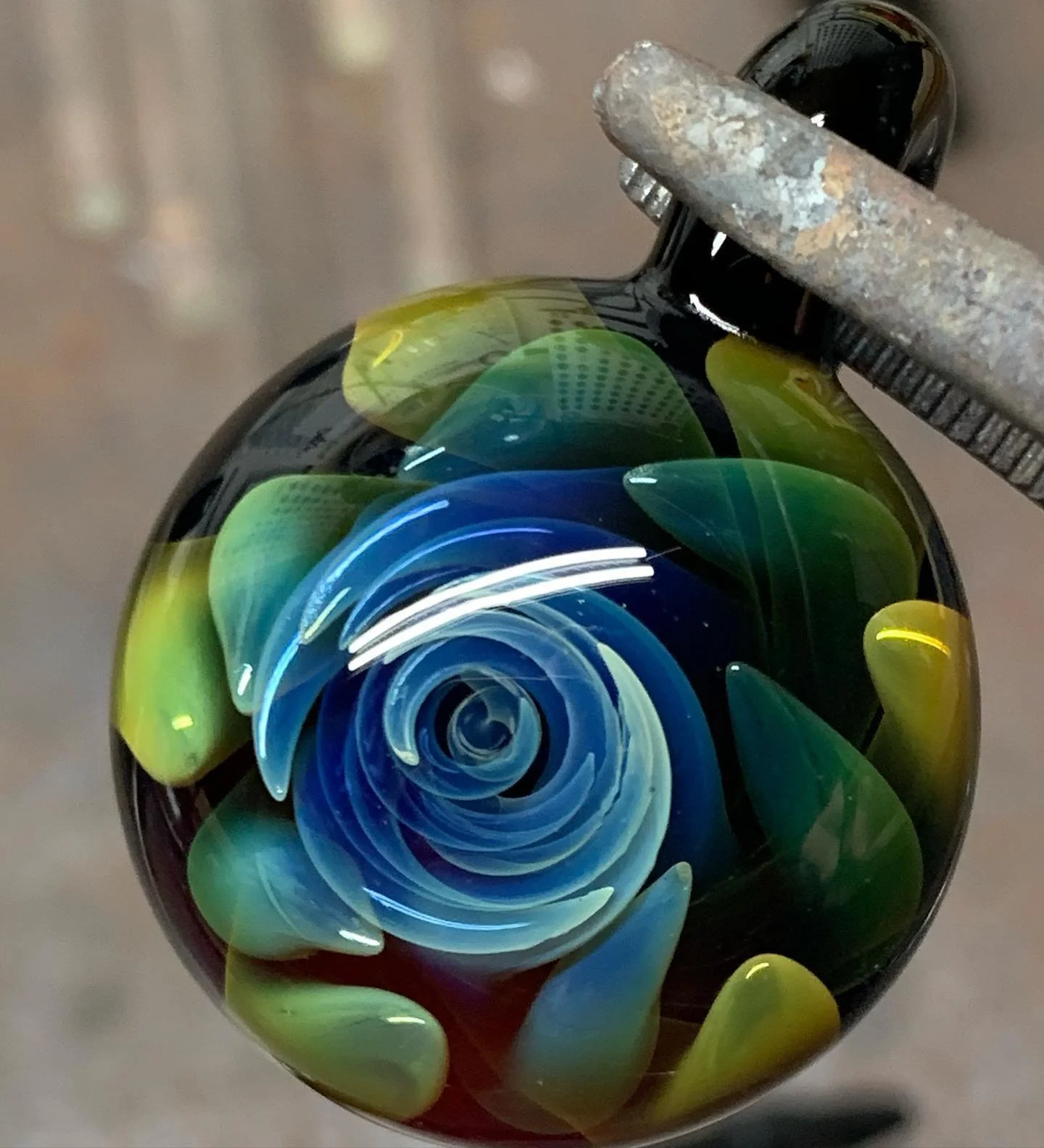Close-up of a colorful glass marble with a swirling pattern of blue, green, and yellow, held by a clamp.