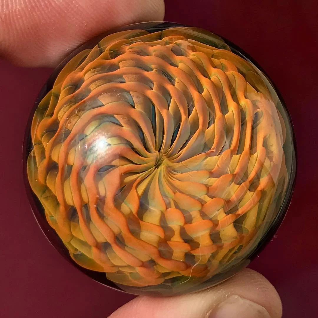 Close-up of a glass marble with a colorful, swirling floral pattern inside.