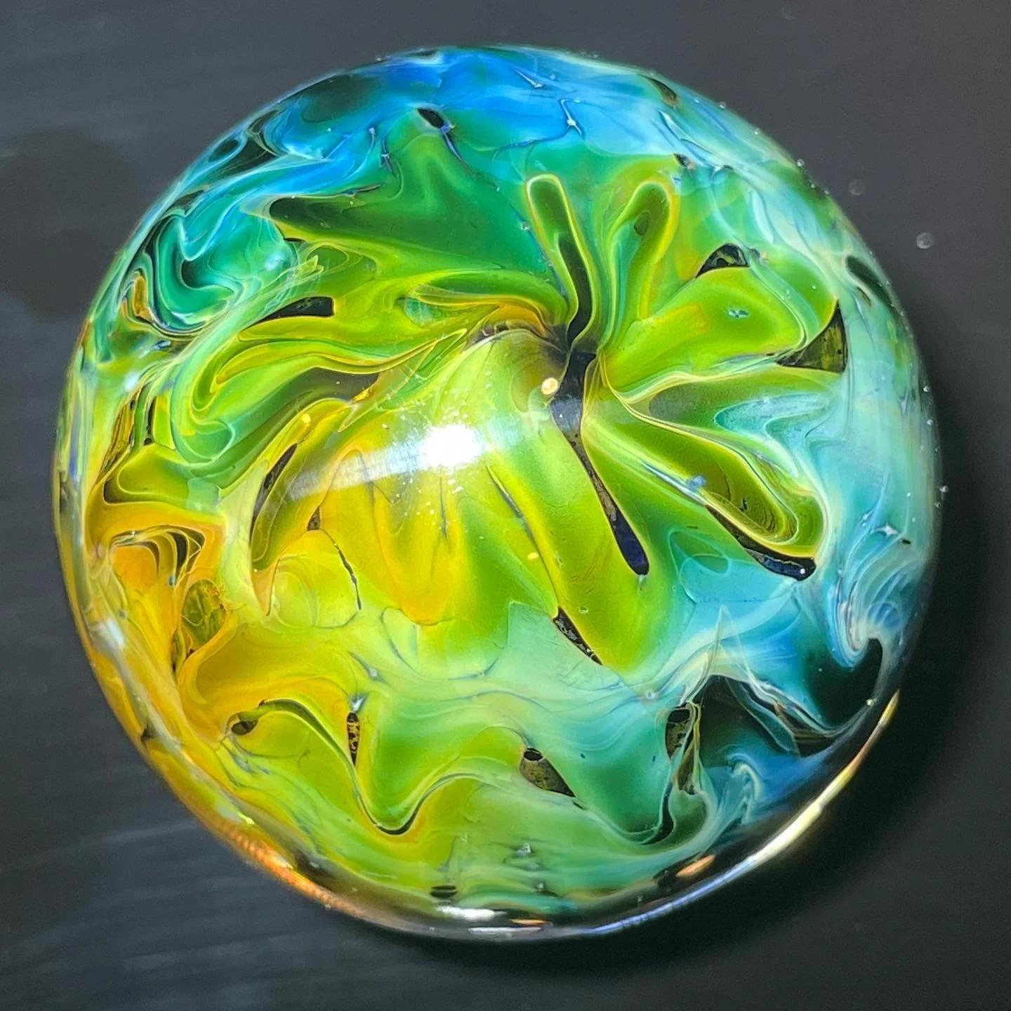 Colorful glass marble with swirls of green, yellow, blue, and black on a black background.