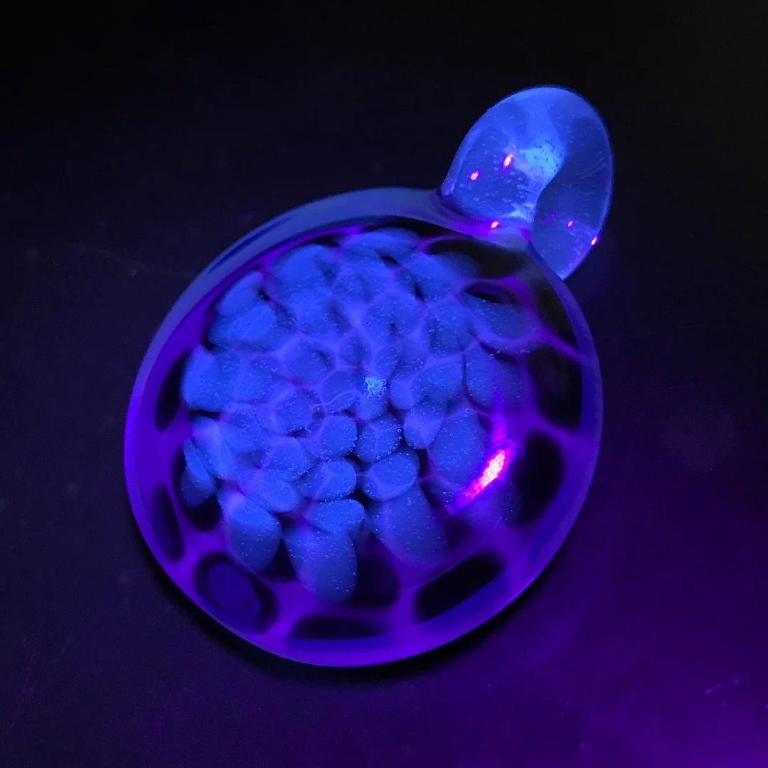 A glass sculpture resembling a bear's head under blacklight, glowing with purple and blue hues, with forms inside that mimic a brain.