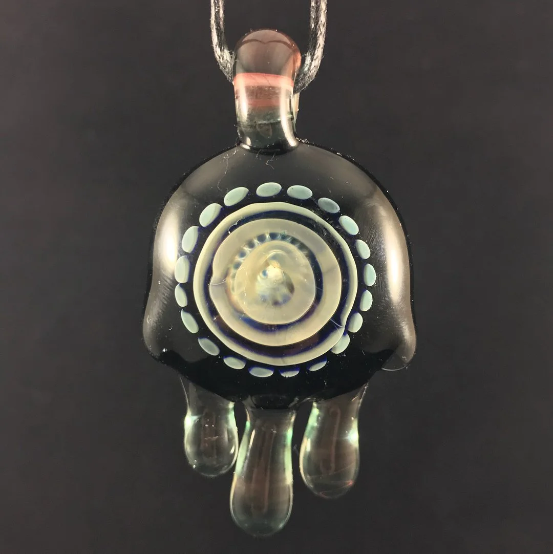 A black glass pendant with white and cream-colored concentric circular patterns and three teardrop-shaped glass drops hanging from the bottom, attached to a silver chain.