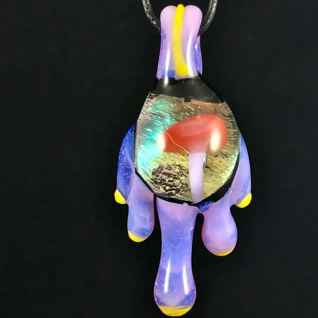 Colorful glass pendant with a mushroom inside, featuring purple, yellow, and blue accents on black background.