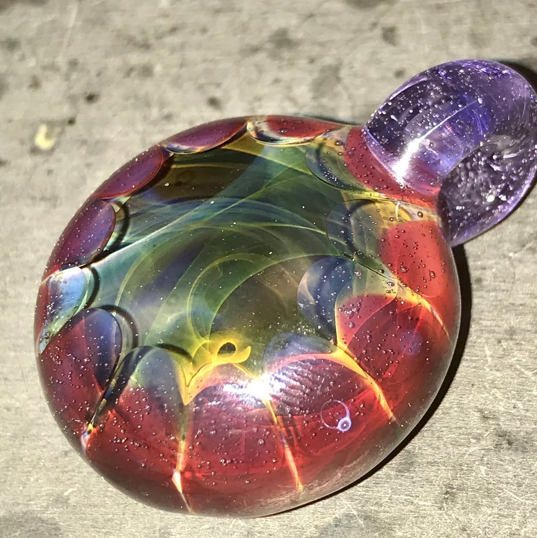 Close-up of a colorful glass pendant with swirling patterns on a textured surface.