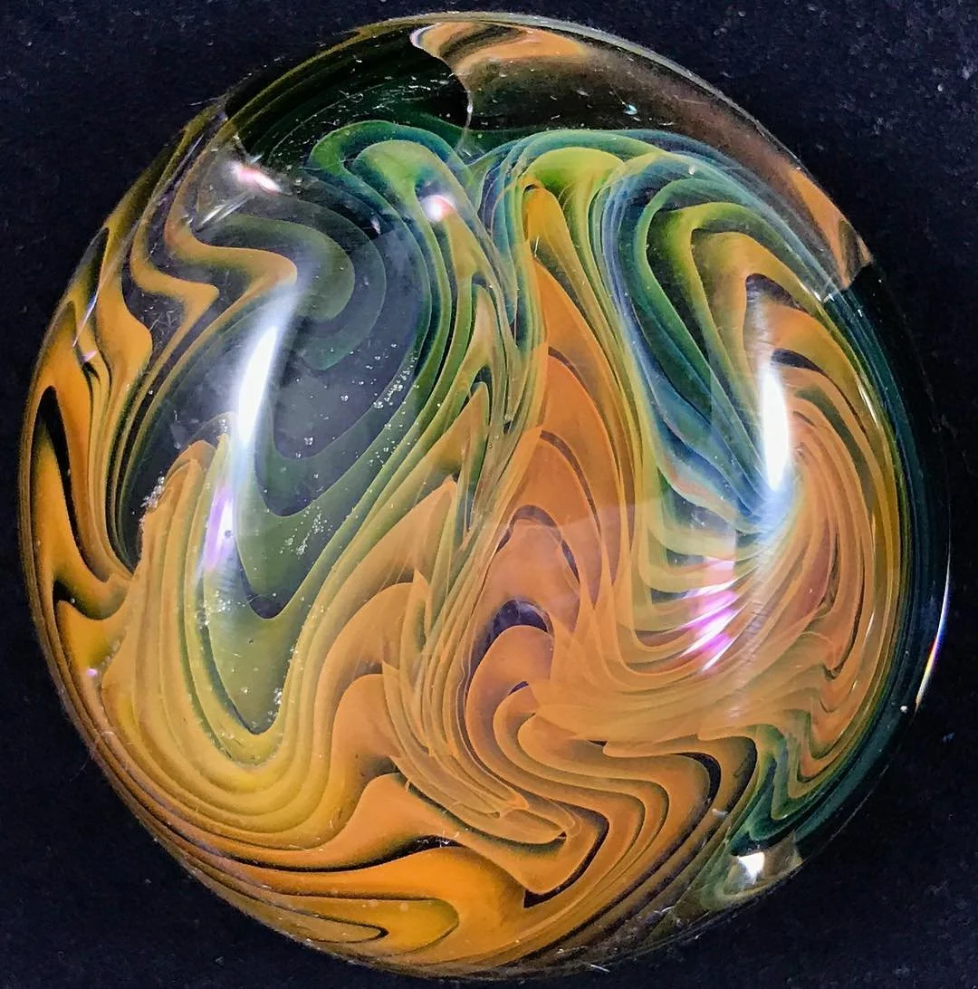 A colorful, swirled glass marble with yellow, green, black, and purple patterns on a dark background.