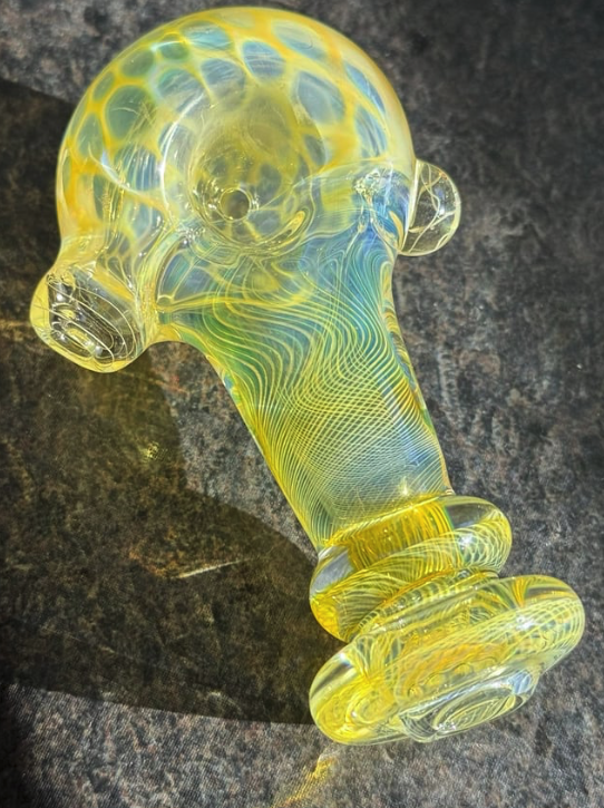 Colorful glass pipe with yellow and blue patterns on a dark surface.