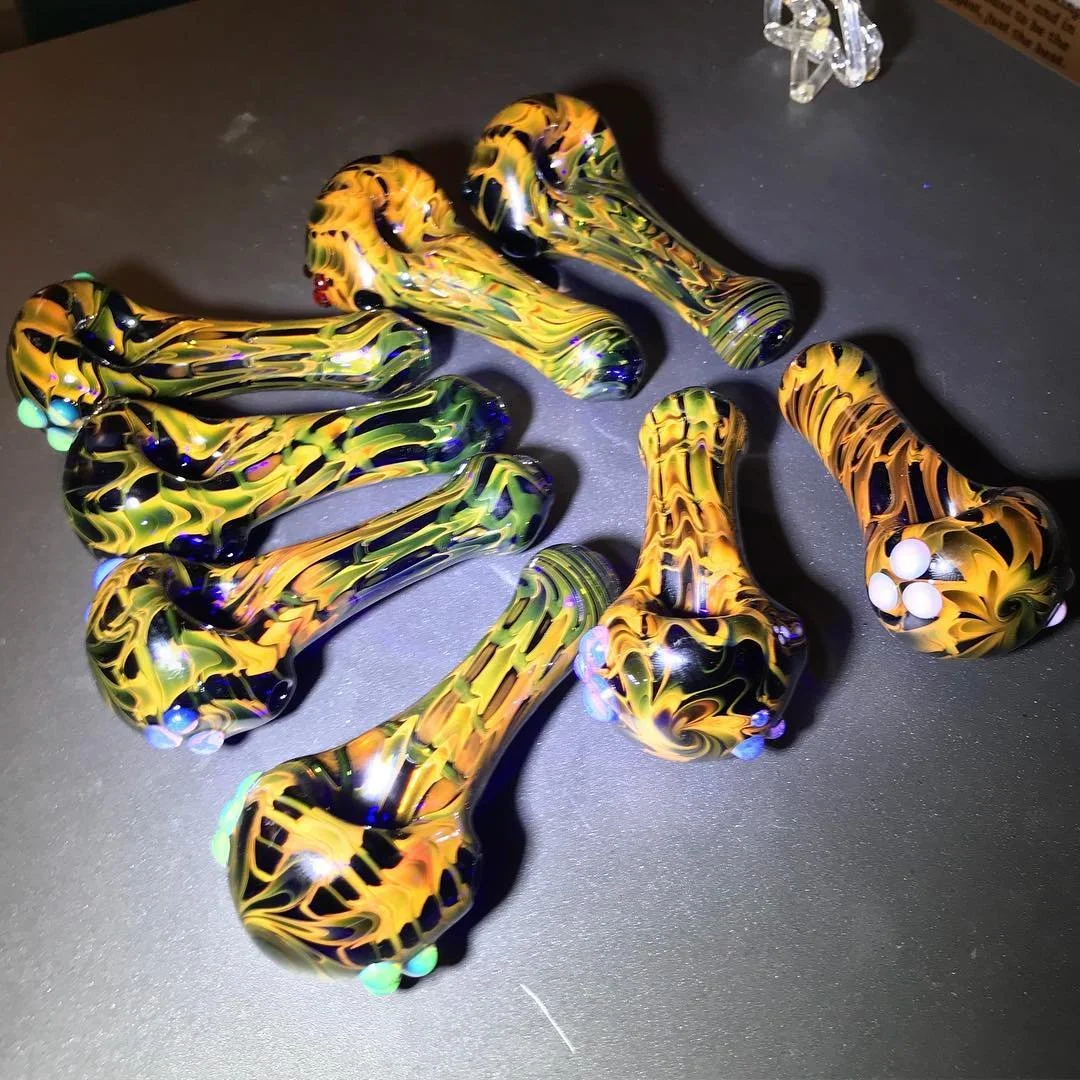 Colorful glass hand pipes with swirls of yellow, black, and green, on a dark surface.