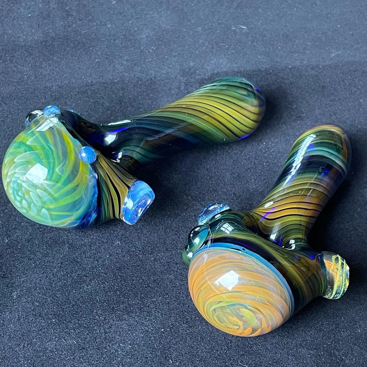 Two colorful, artistic glass pipes with swirling patterns, lying on a dark surface.