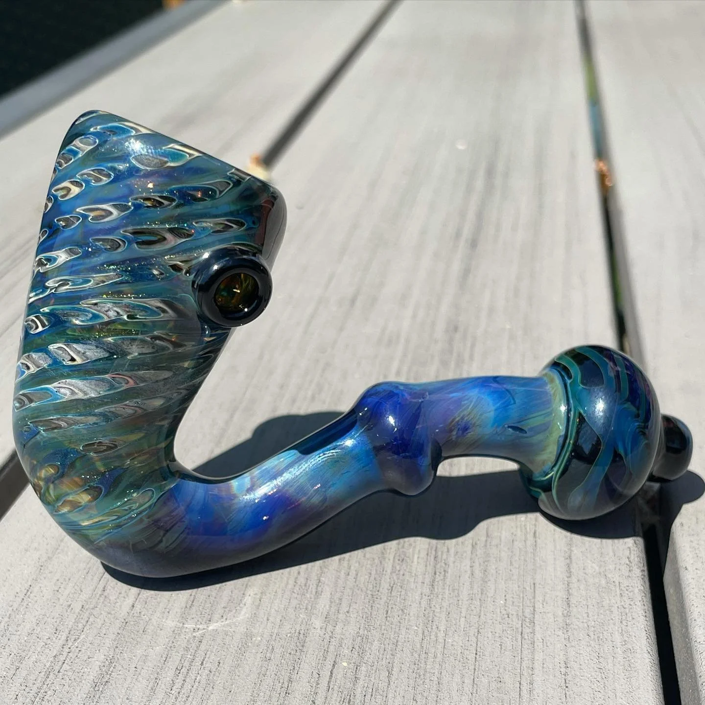 A colorful glass pipe with swirling blue, green, and yellow patterns resting on a light gray wooden surface.