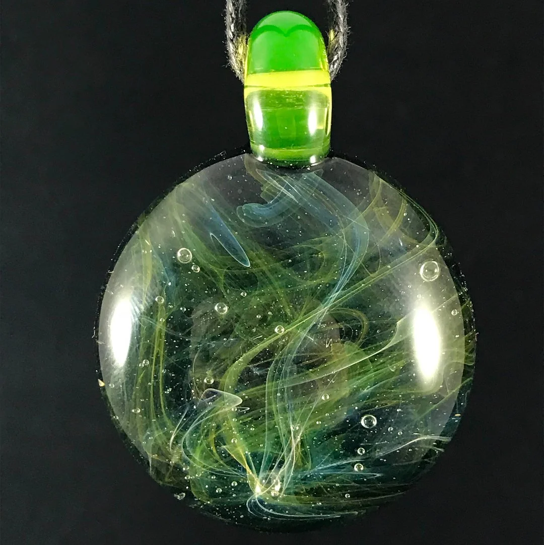 A glass pendant with swirling green and blue patterns inside against a black background.