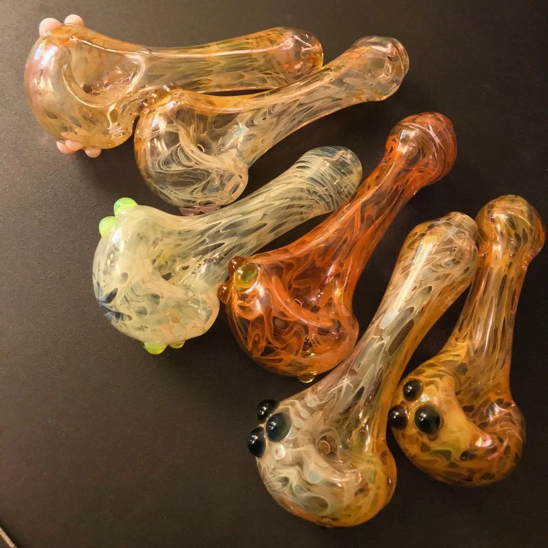 Several hand-blown glass pipes with swirled amber, cream, and black colors on a black background.