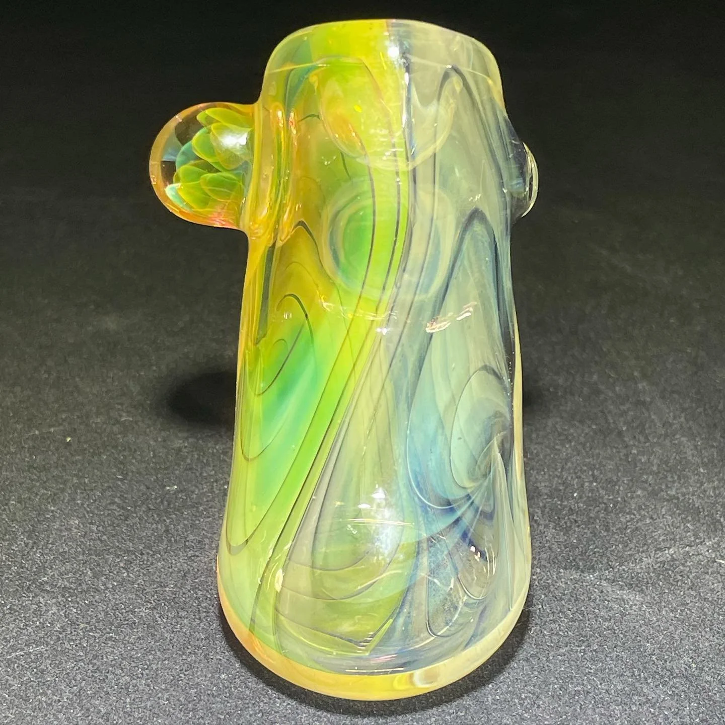 Colorful glass pipe with swirling yellow, green, and blue patterns on a black surface.