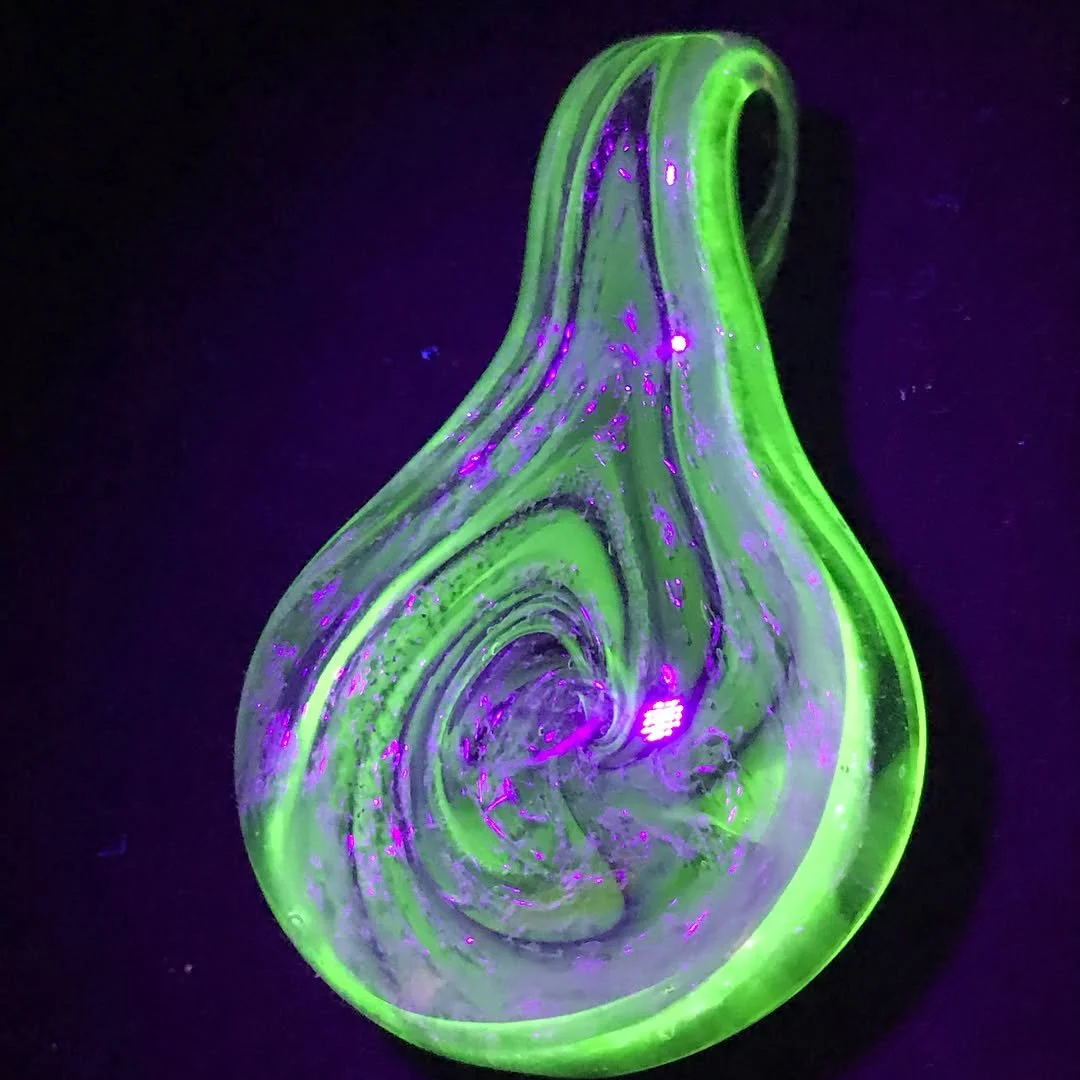 Green and purple glowing glass pendant with a teardrop shape, set against a black background.