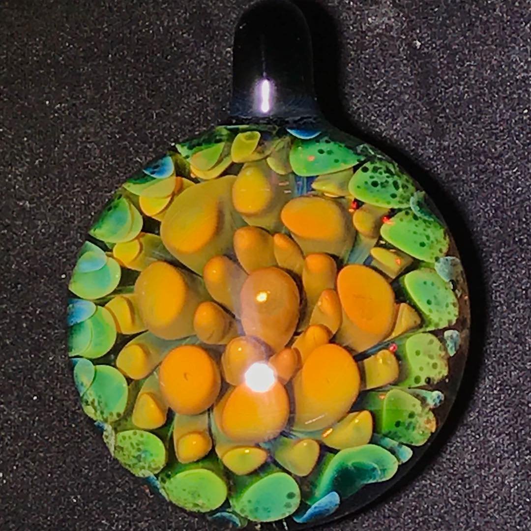 Colorful glass pendant with yellow and green bubbles on a black background.
