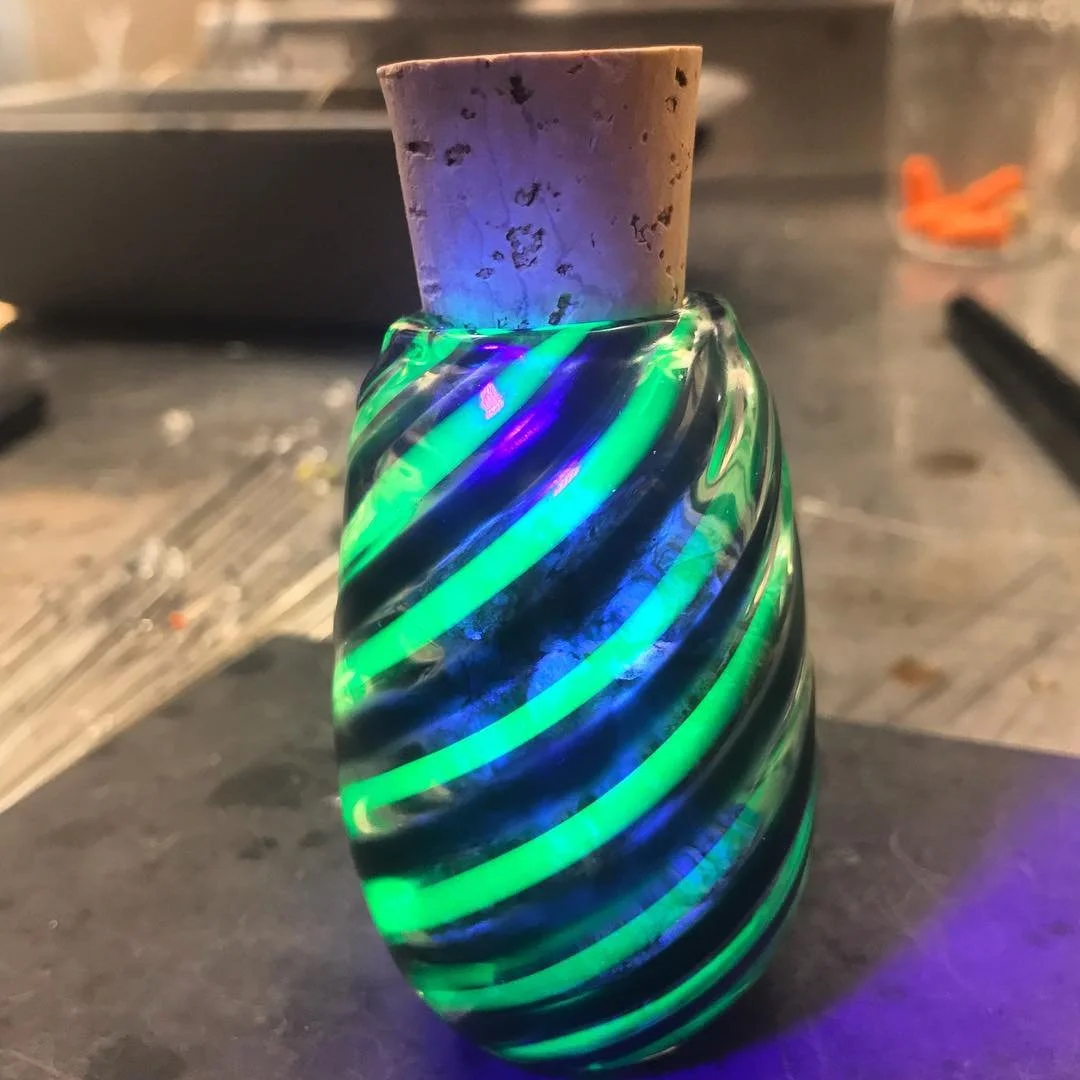 A glass vase with green and blue spiraling stripes and a cork stopper on top.