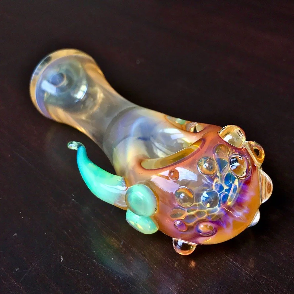 Colorful glass art pipe with a curvy shape and bubble-like textures, resting on a dark surface.