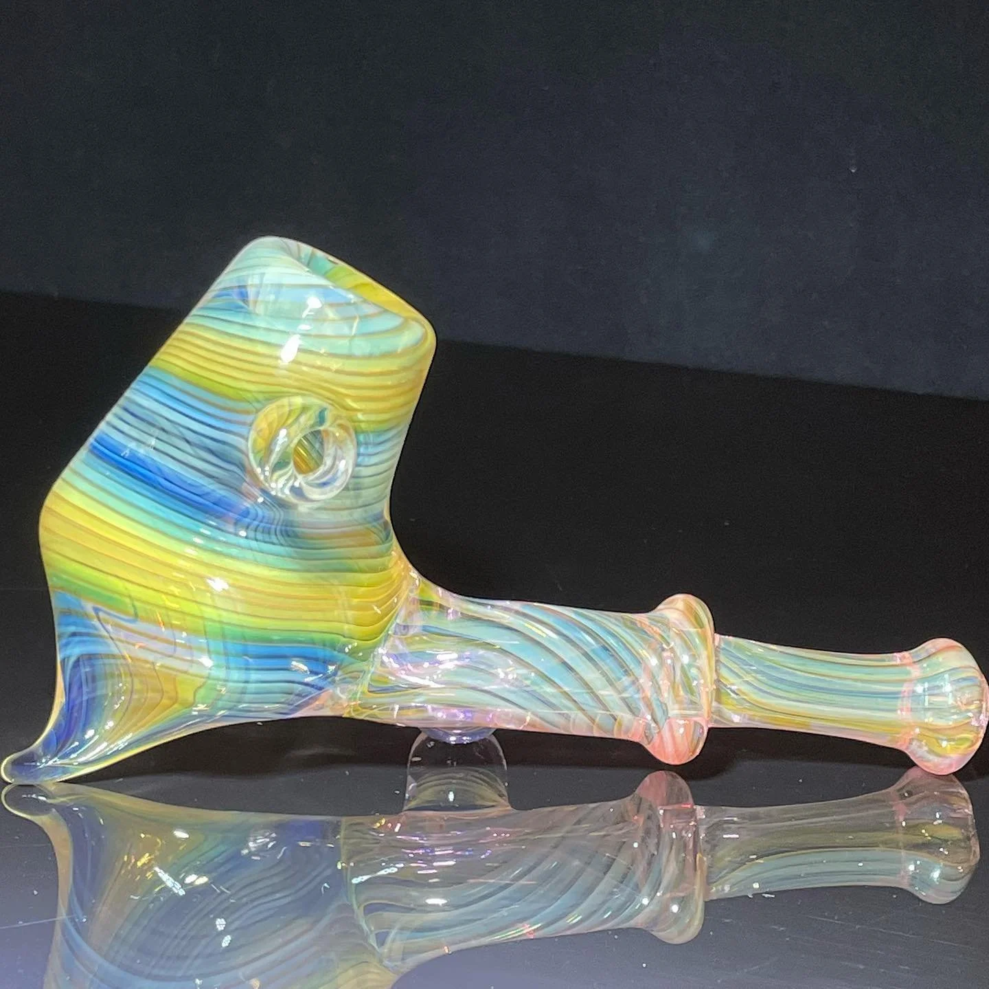 Colorful, iridescent glass pipe with a curved body and a round bowl, resting on a reflective black surface.