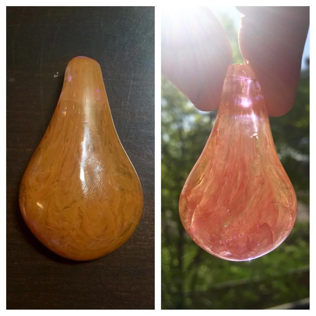 A wooden and a glass teardrop-shaped object, with the wooden one displayed on a dark surface and the glass one held outdoors with sunlight shining through.