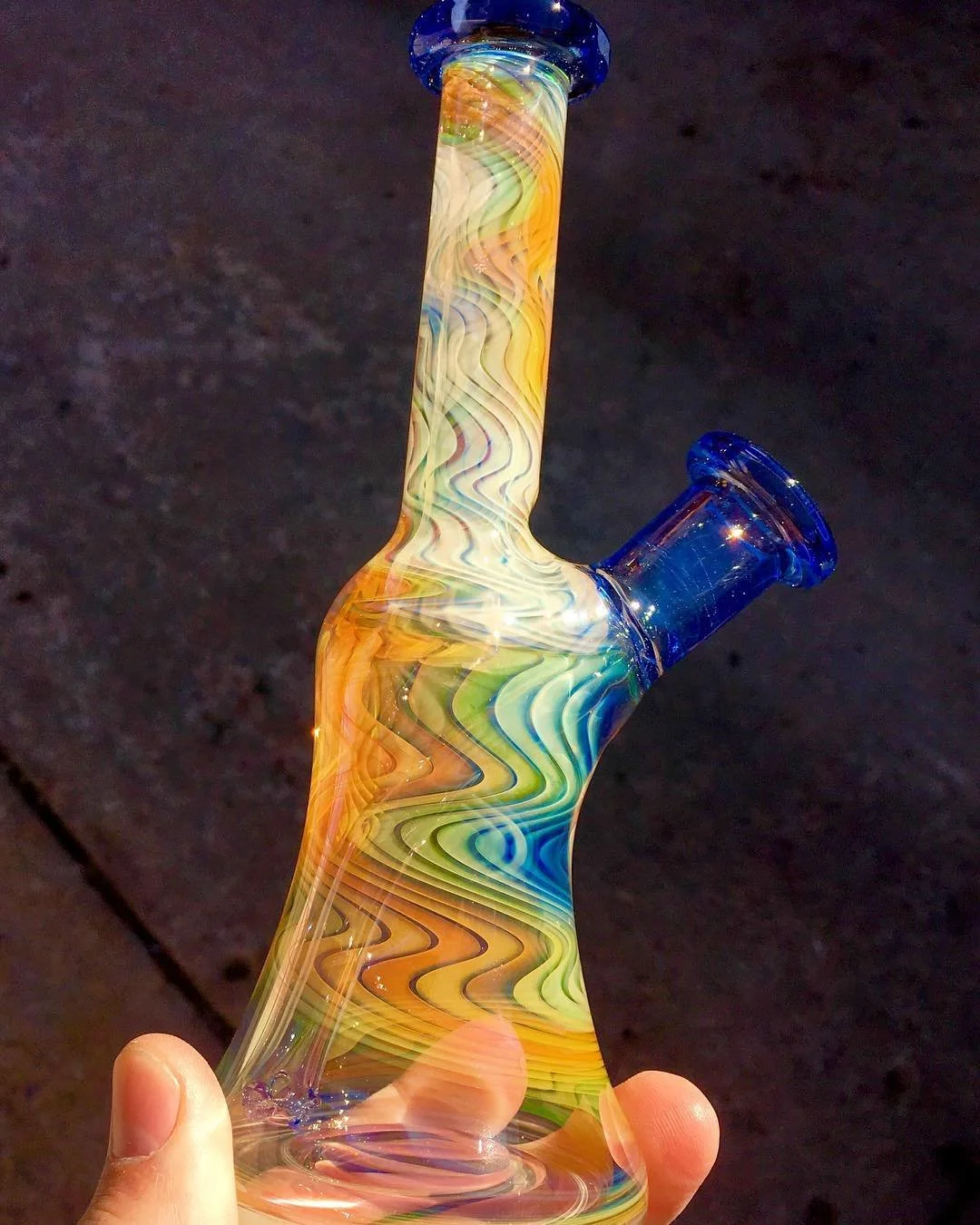 Colorful glass pipe with swirling patterns, held in a person's hand against a dark background.