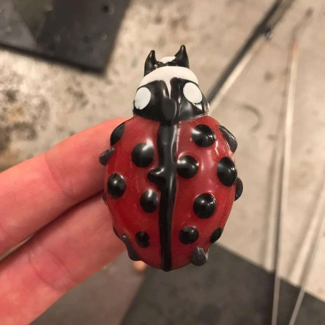 A small decorative figurine of a ladybug being held between a person's thumb and index finger.