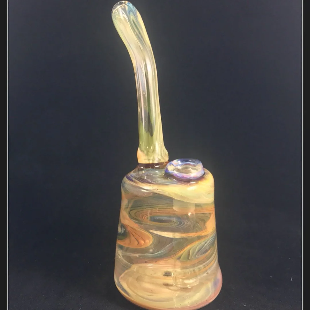 A small, colorful glass sculpture with a twisted, elongated top on a dark background.