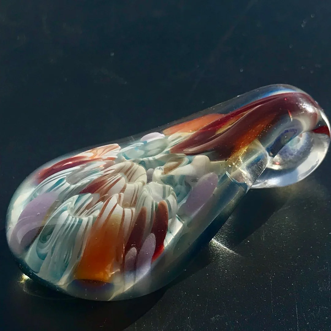 Close-up of a colorful glass pendant with swirled patterns in red, orange, blue, and white, on a dark surface.