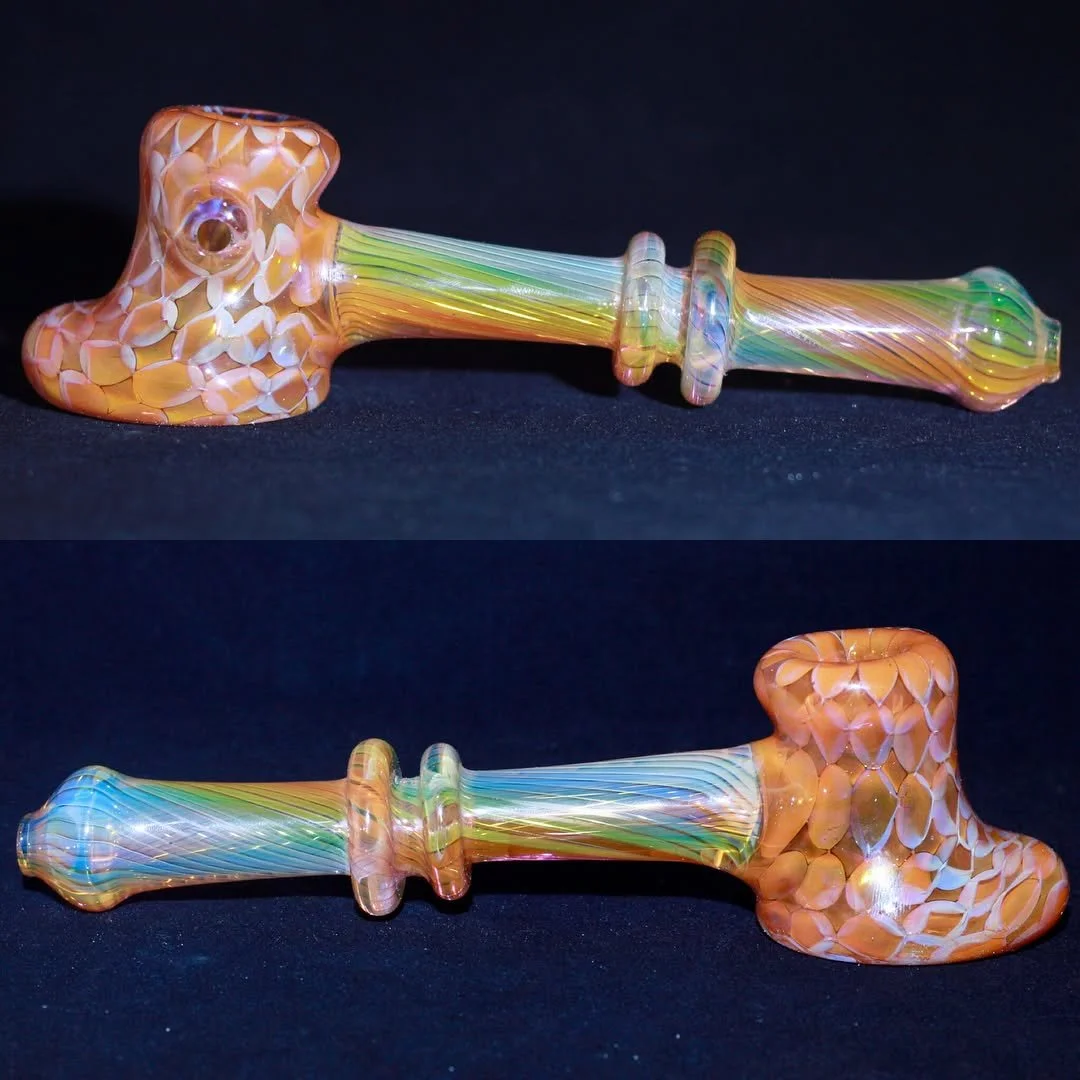 Gold and silver fumed Colorful glass pipe with a mosaic design on the bowl and rainbow stripes on the stem, lying on a black surface.