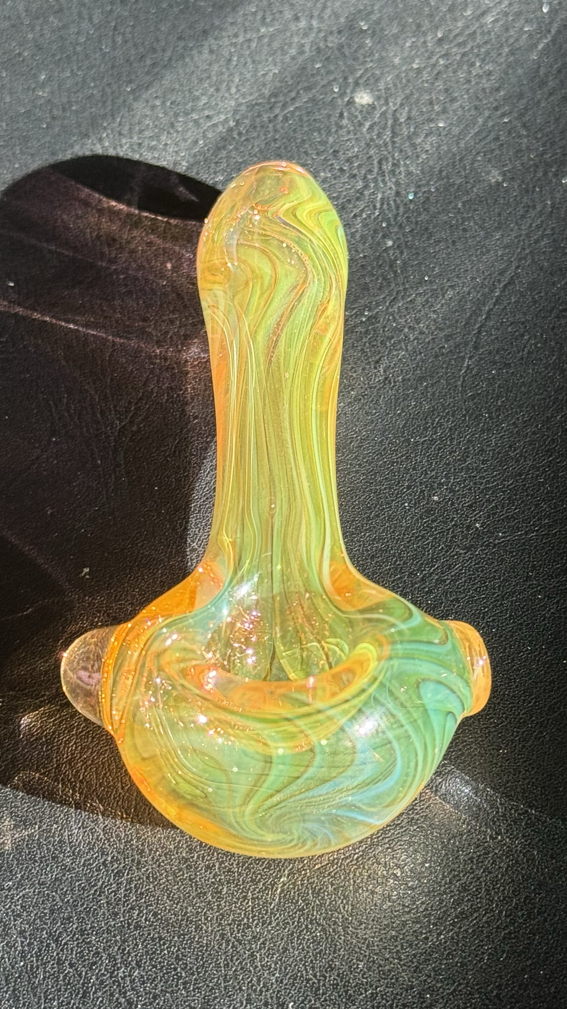 A colorful, swirled glass pipe with shades of yellow, green, and orange on a black surface.