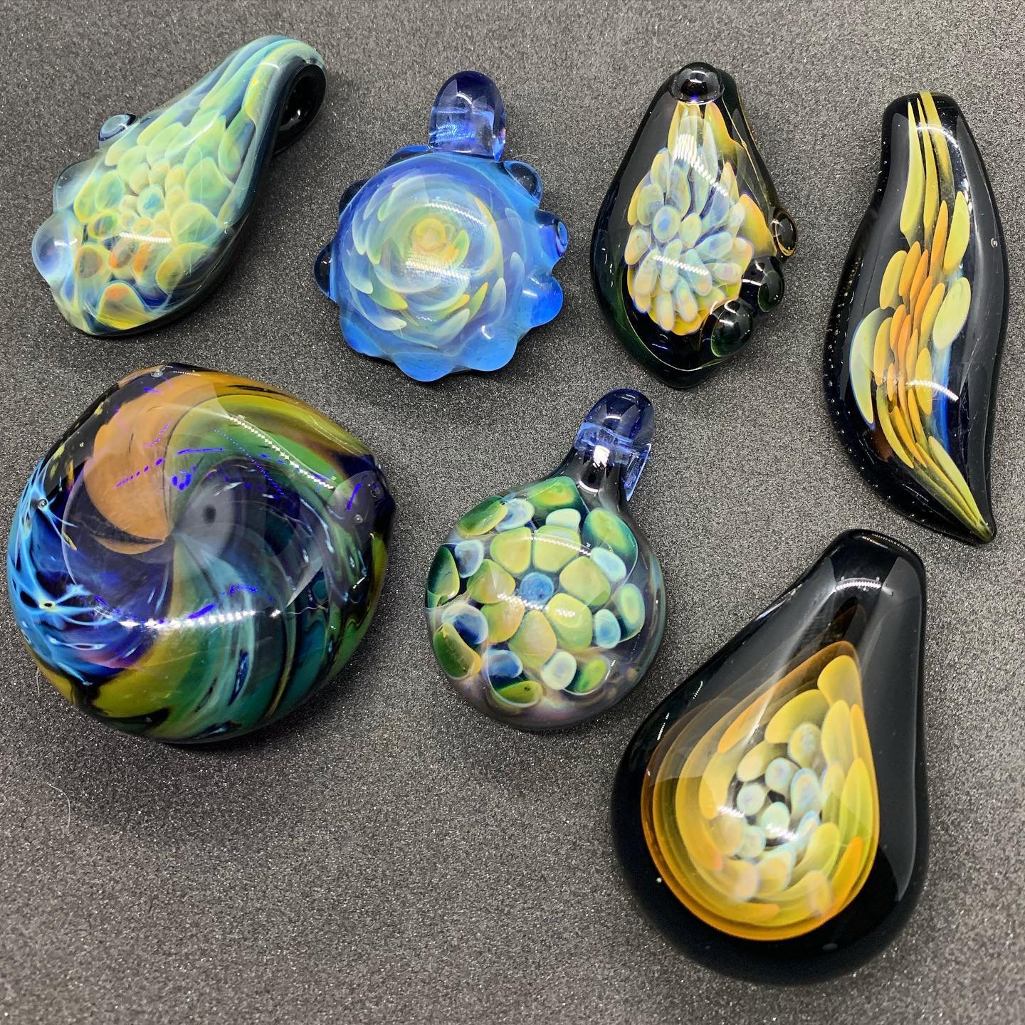 Collection of colorful handcrafted glass art pieces, including various shapes and sizes on a black surface.