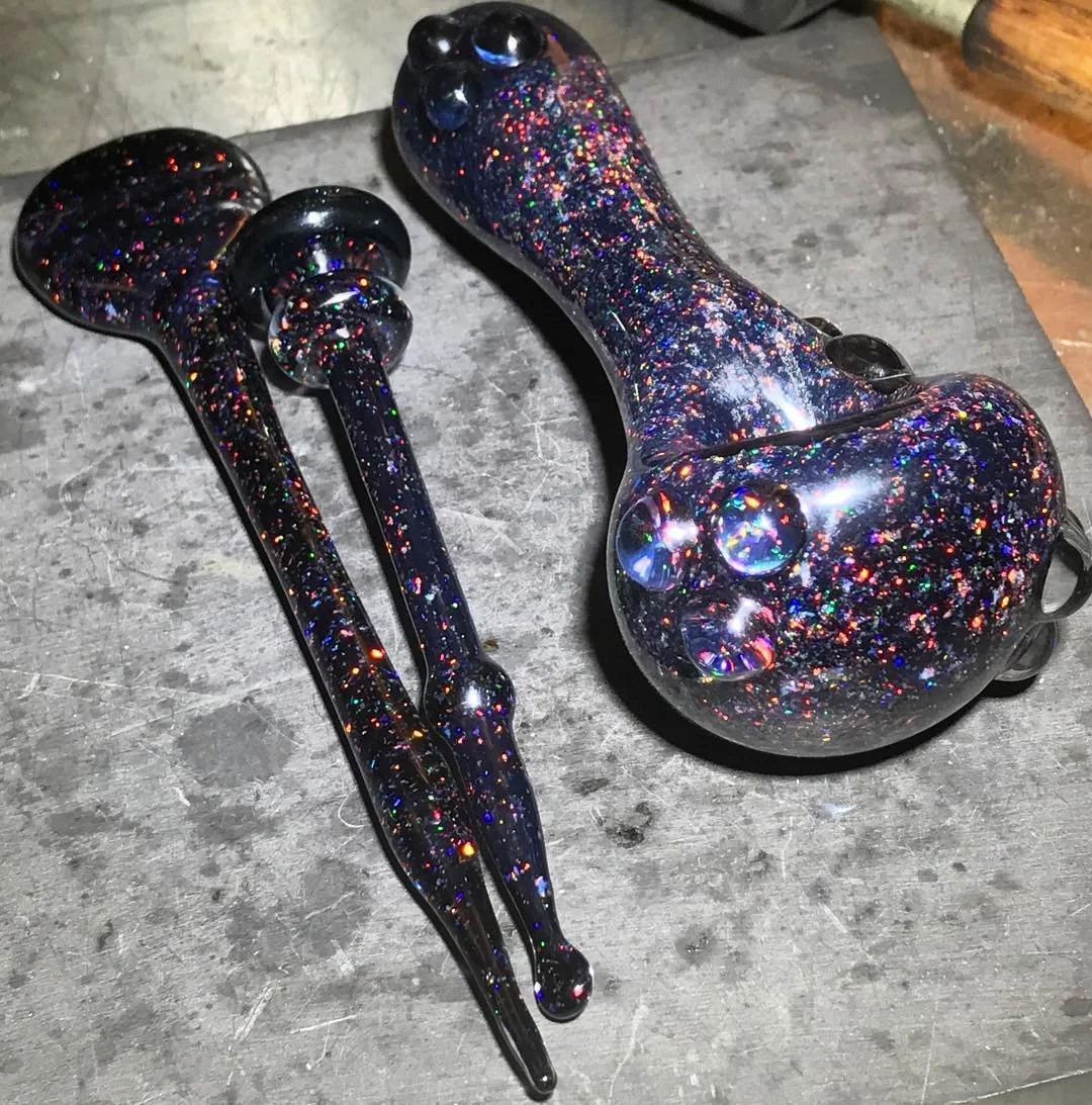 A pair of black hair clips and a black hair roller with multicolored glitter on a gray surface.