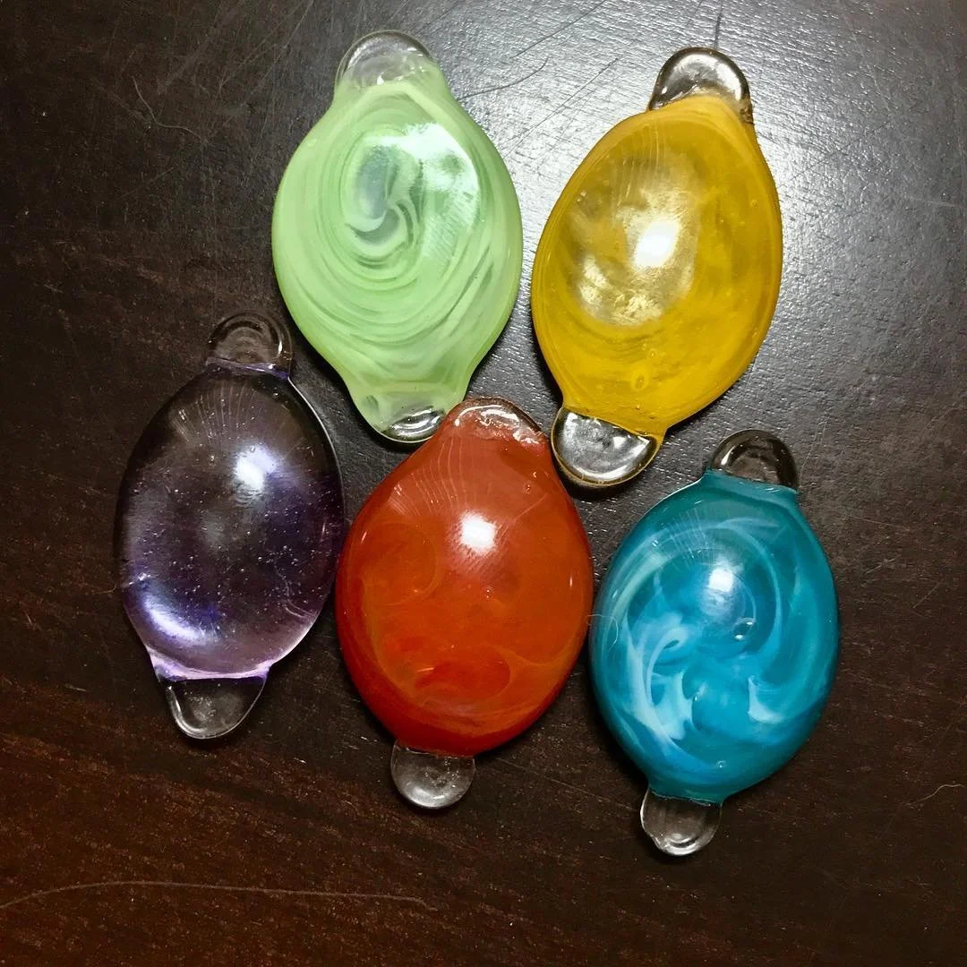 Five colorful glass stones on a dark wooden surface, arranged in a semi-circle. The stones are purple, green, yellow, orange, and blue.