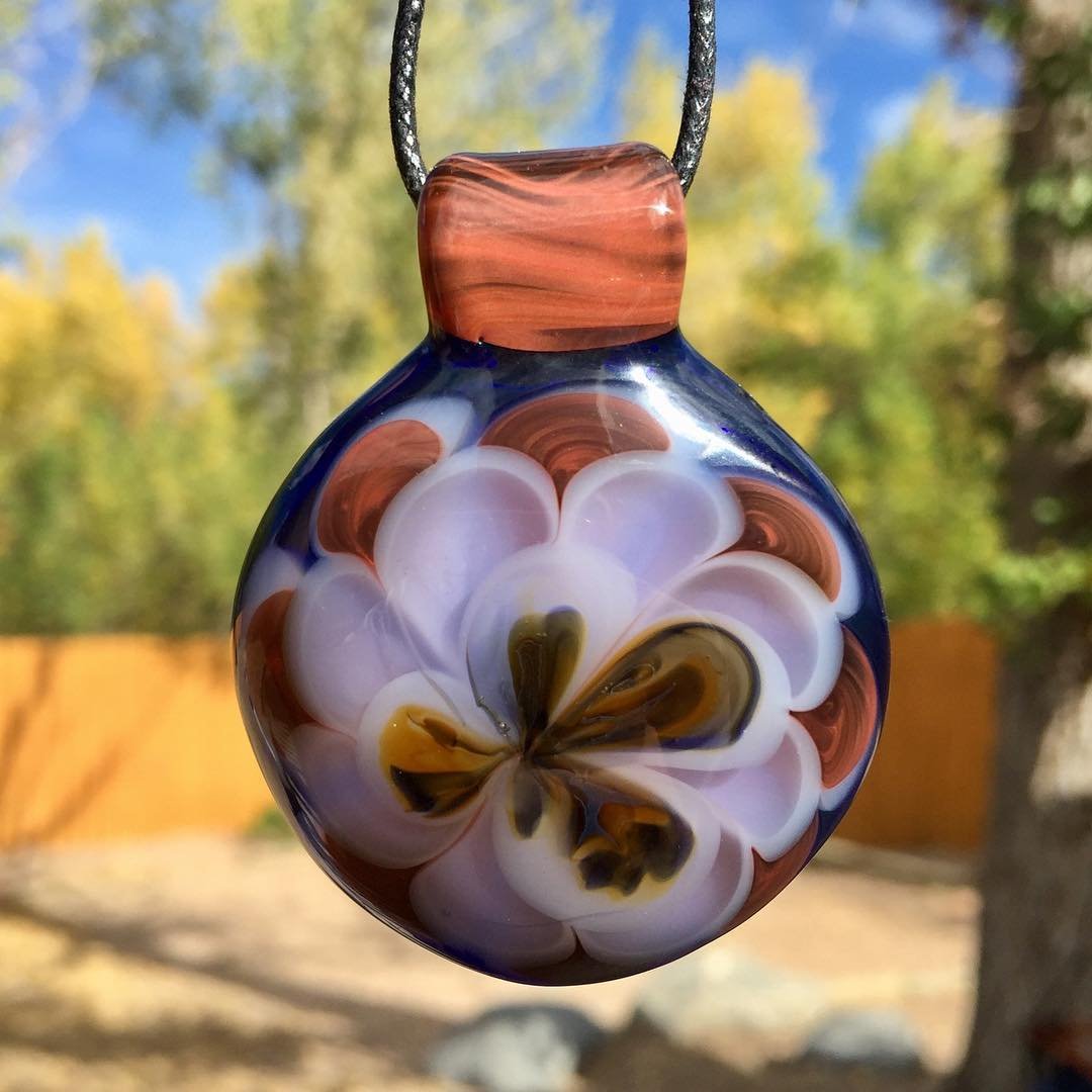 Colorful glass pendant with a floral design, hanging outdoors with trees and a blue sky in the background.