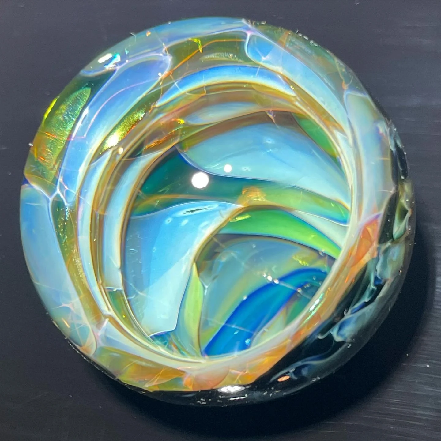 A colorful glass paperweight with swirls of blue, green, yellow, and orange, resting on a dark surface.