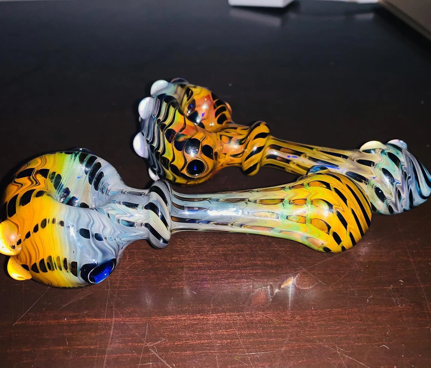 Colorful glass pipes with yellow, black, white, and blue patterns on a wooden surface.