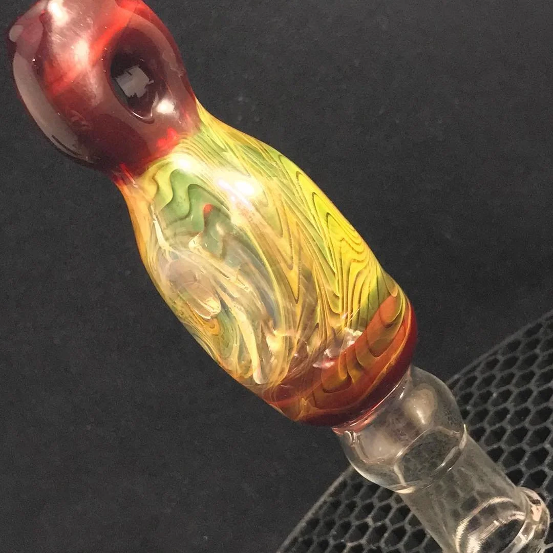 A colorful glass pipe with a swirl of red, yellow, green, and orange colors, resting on a black surface.