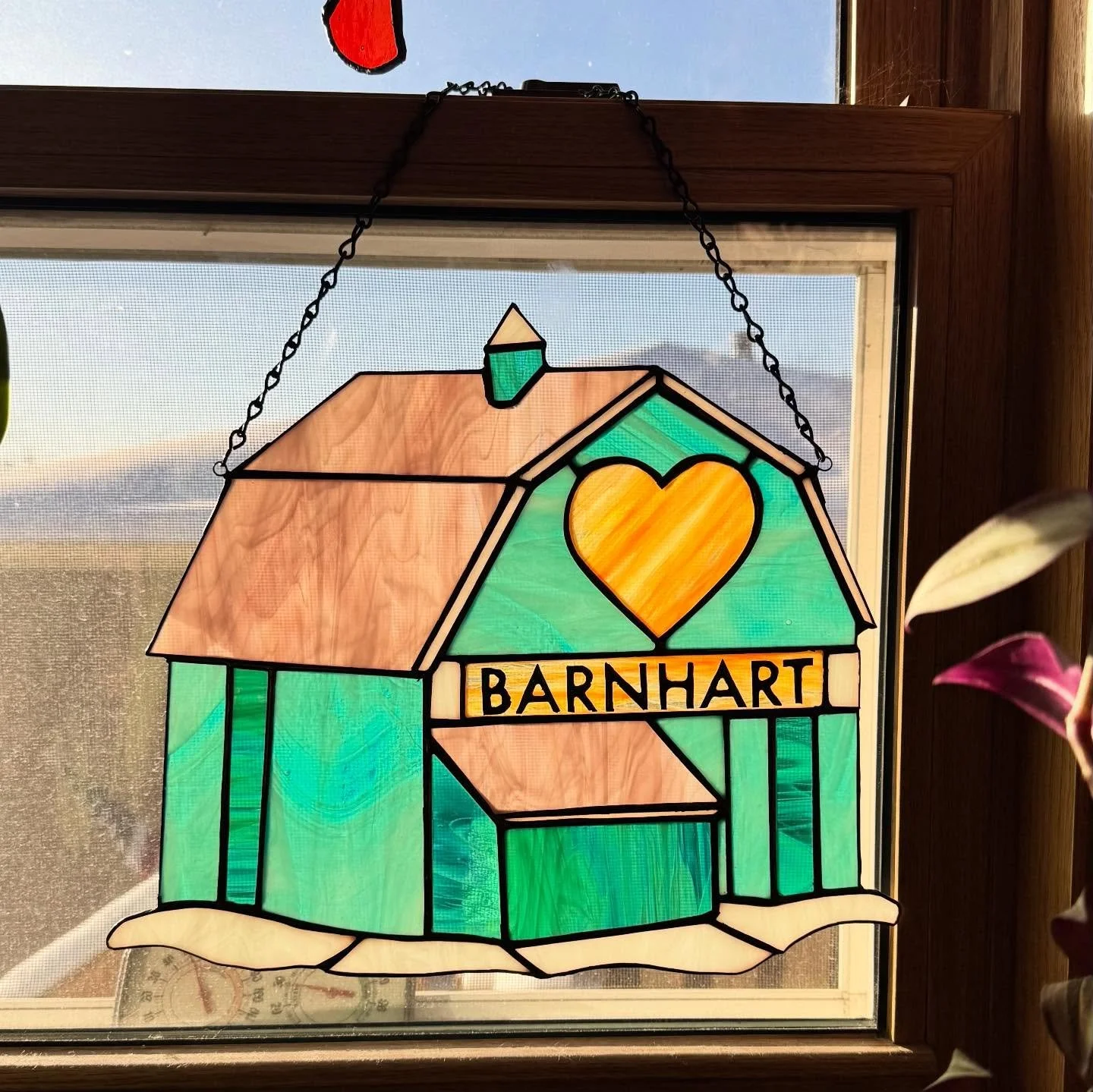 Stained glass window art of a house with a heart, a chimney, and the word 'BARNHART' on a banner.