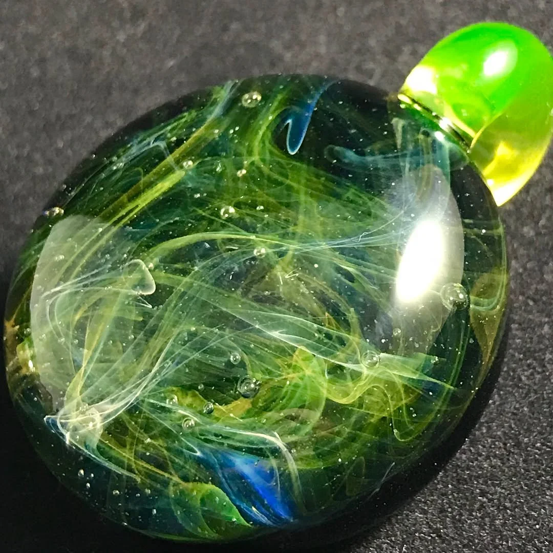Photograph of a glass marble with swirling green, blue, and yellow colors inside on a dark surface.