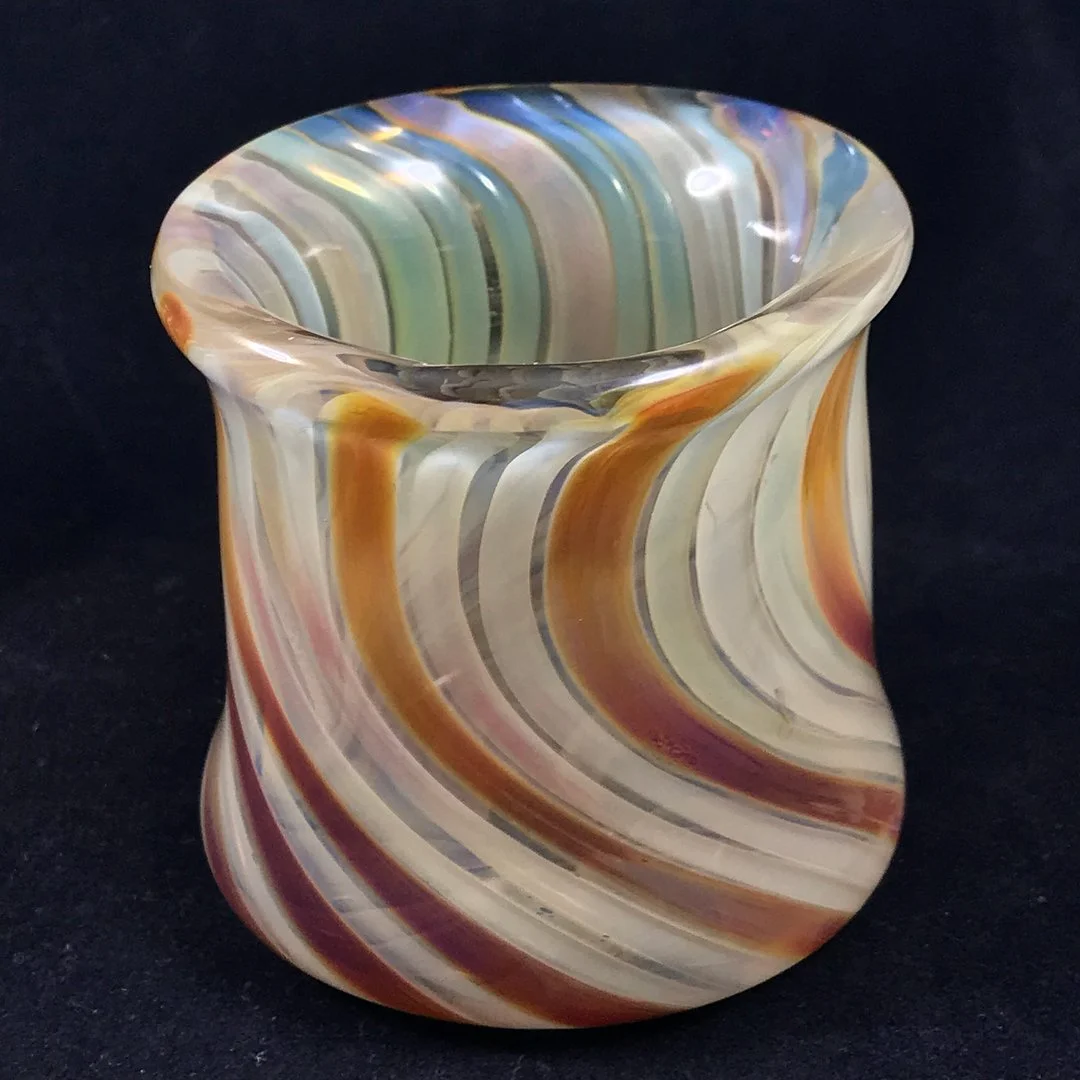 Colorful swirl glass vase with orange, beige, green, and blue stripes on a black background.
